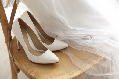 Photo of Pair of white wedding high heel shoes and veil on wooden chair indoors