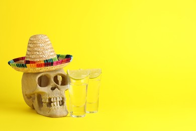 Photo of Human scull with Mexican sombrero hat, tequila in glasses and lime on yellow background, space for text