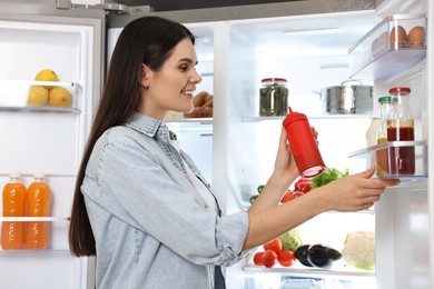 Photo of Young woman taking bottle of ketchup out of refrigerator
