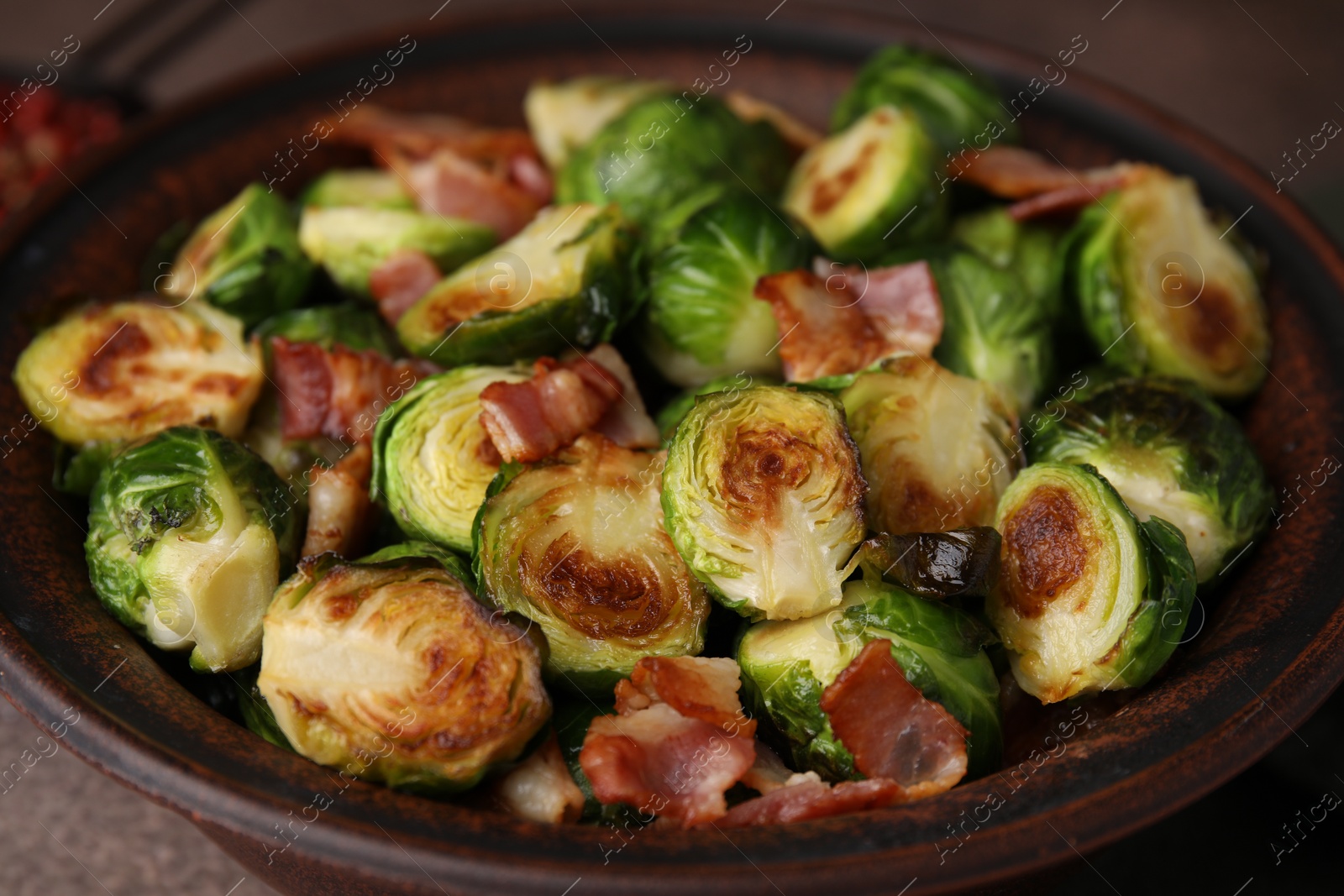 Photo of Delicious roasted Brussels sprouts and bacon in bowl on table, closeup