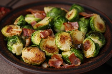 Delicious roasted Brussels sprouts and bacon in bowl on table, closeup