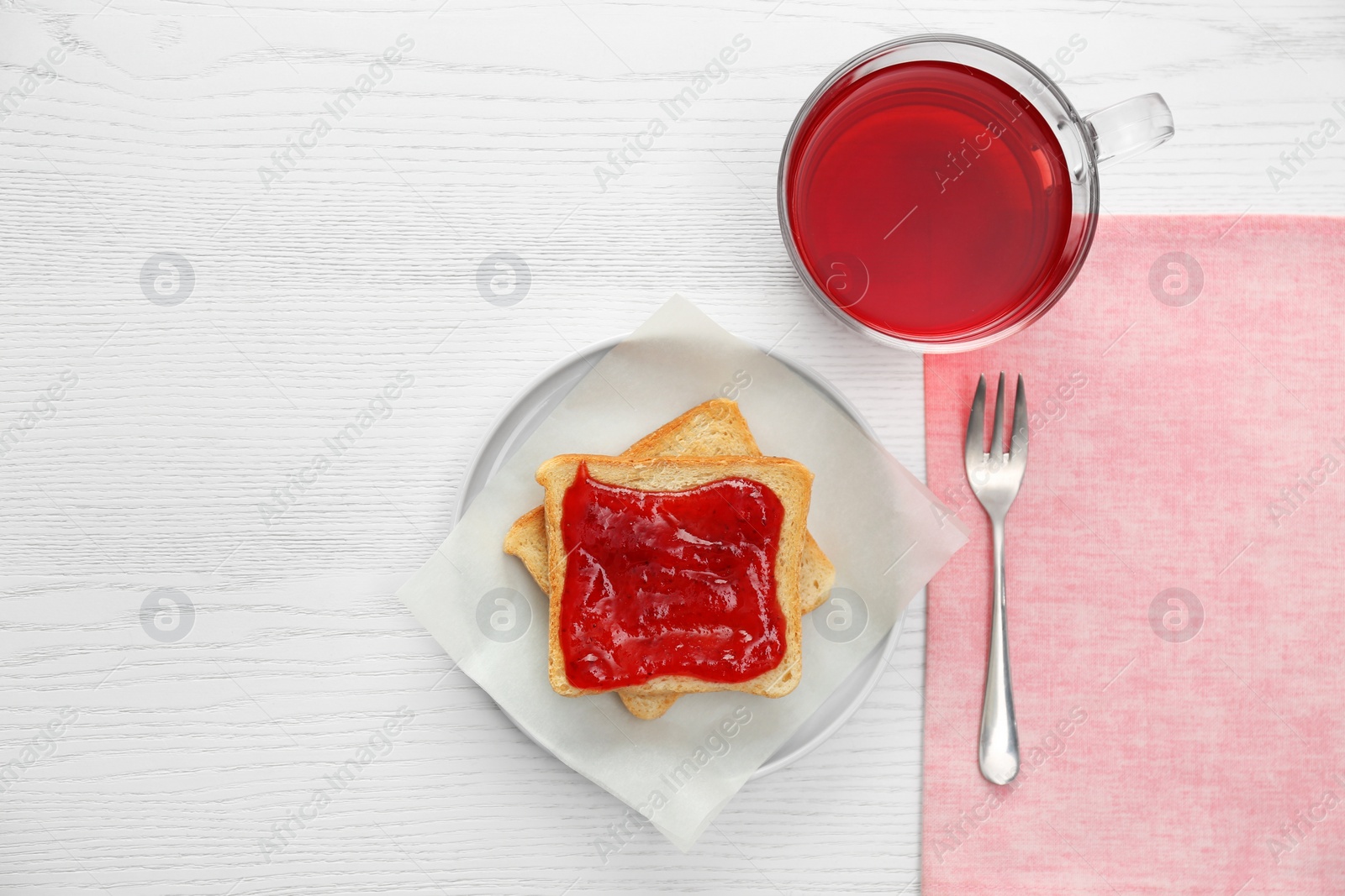 Photo of Tasty toast with jam and raspberry tea on white wooden table, flat lay. Delicious morning meal