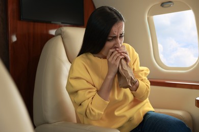 Nervous young woman with aviophobia breathing into paper bag in airplane