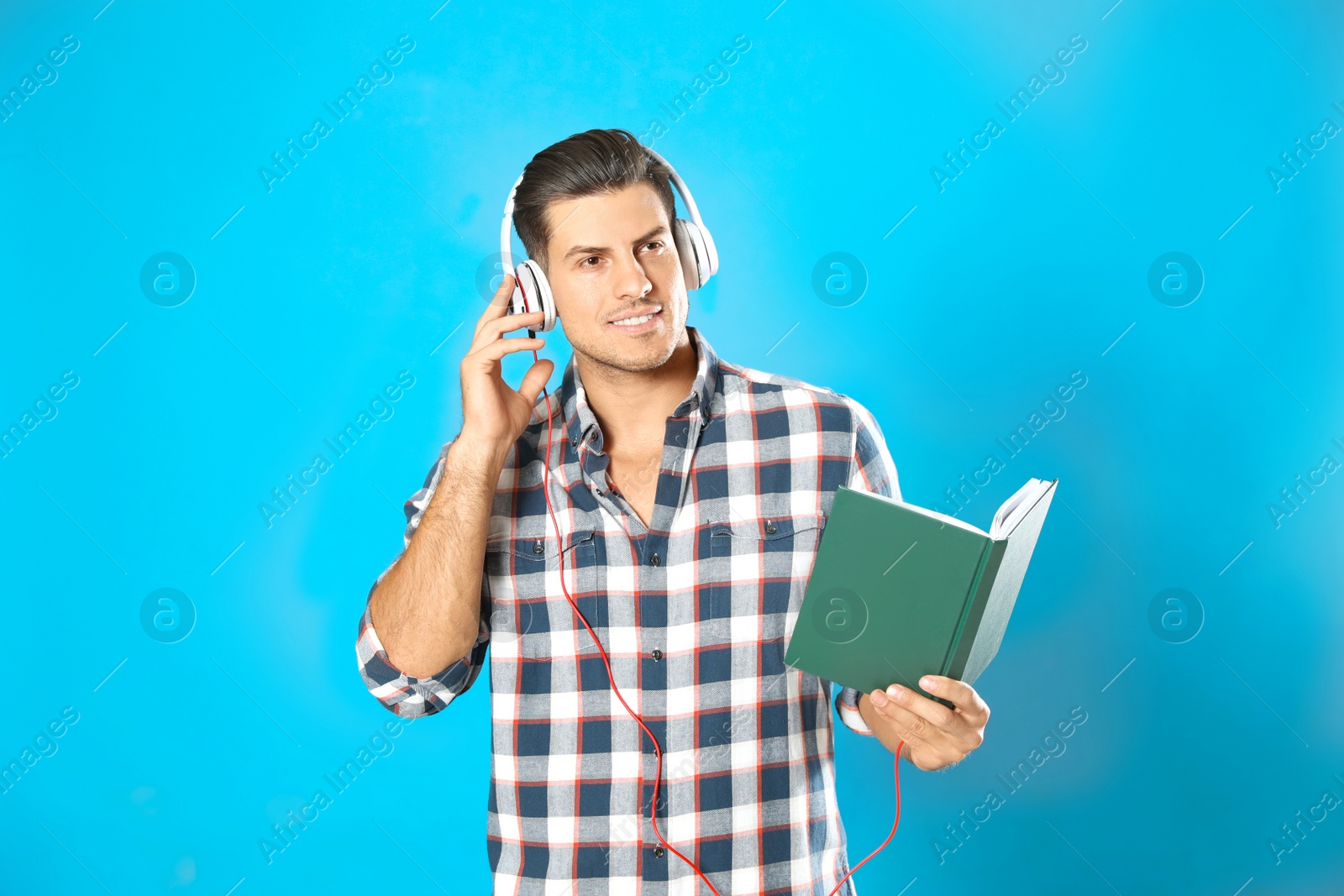 Photo of Man with headphones and book on light blue background. Audiobook concept