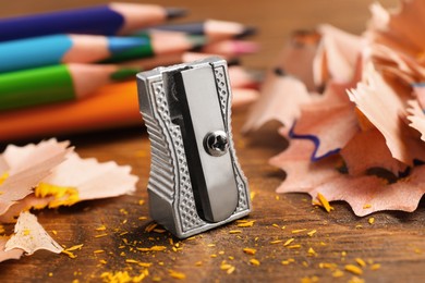 Photo of Metal sharpener, colorful graphite crumbs and pencils on wooden table, closeup