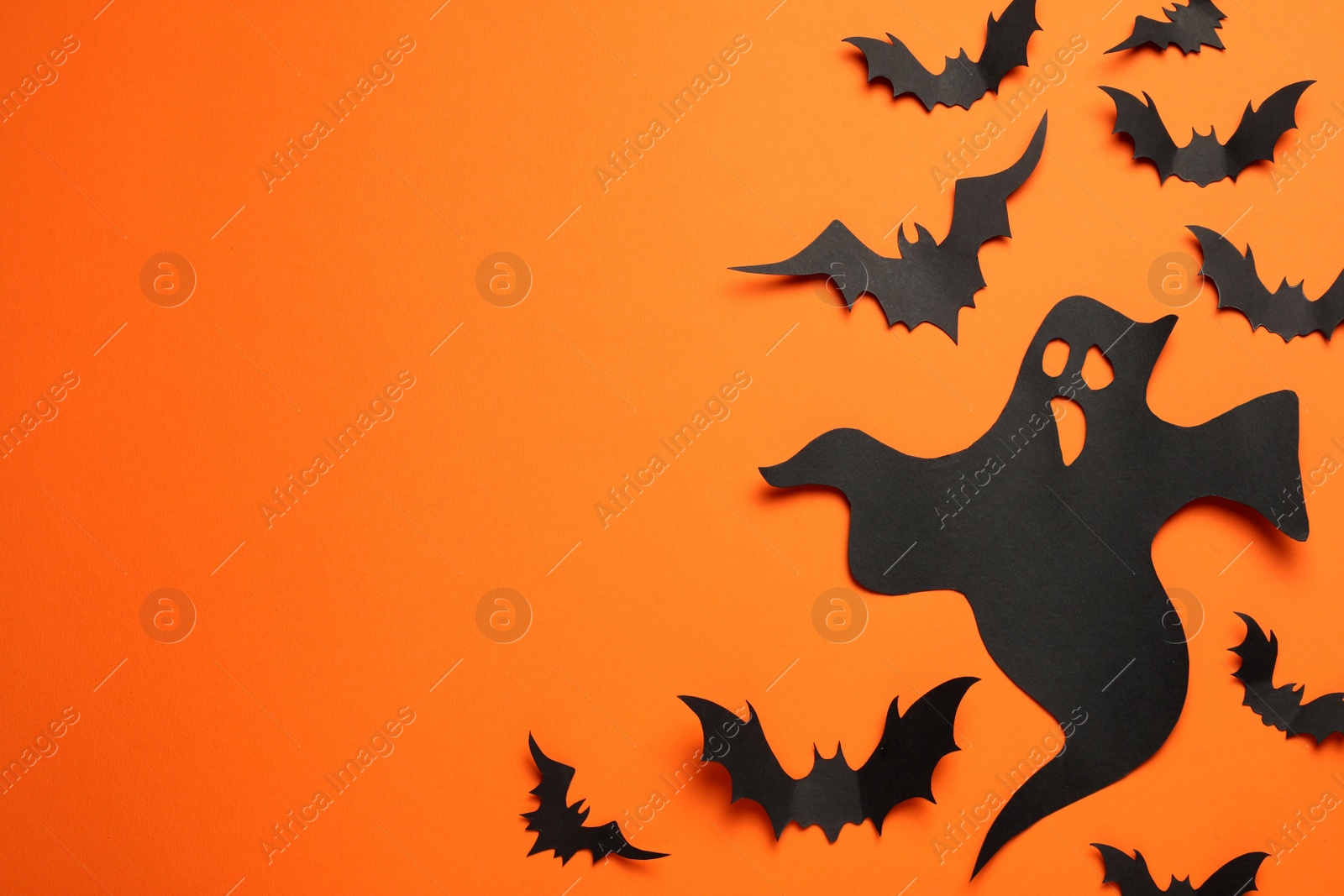 Photo of Flat lay composition with paper ghost and bats on orange background, space for text. Halloween celebration