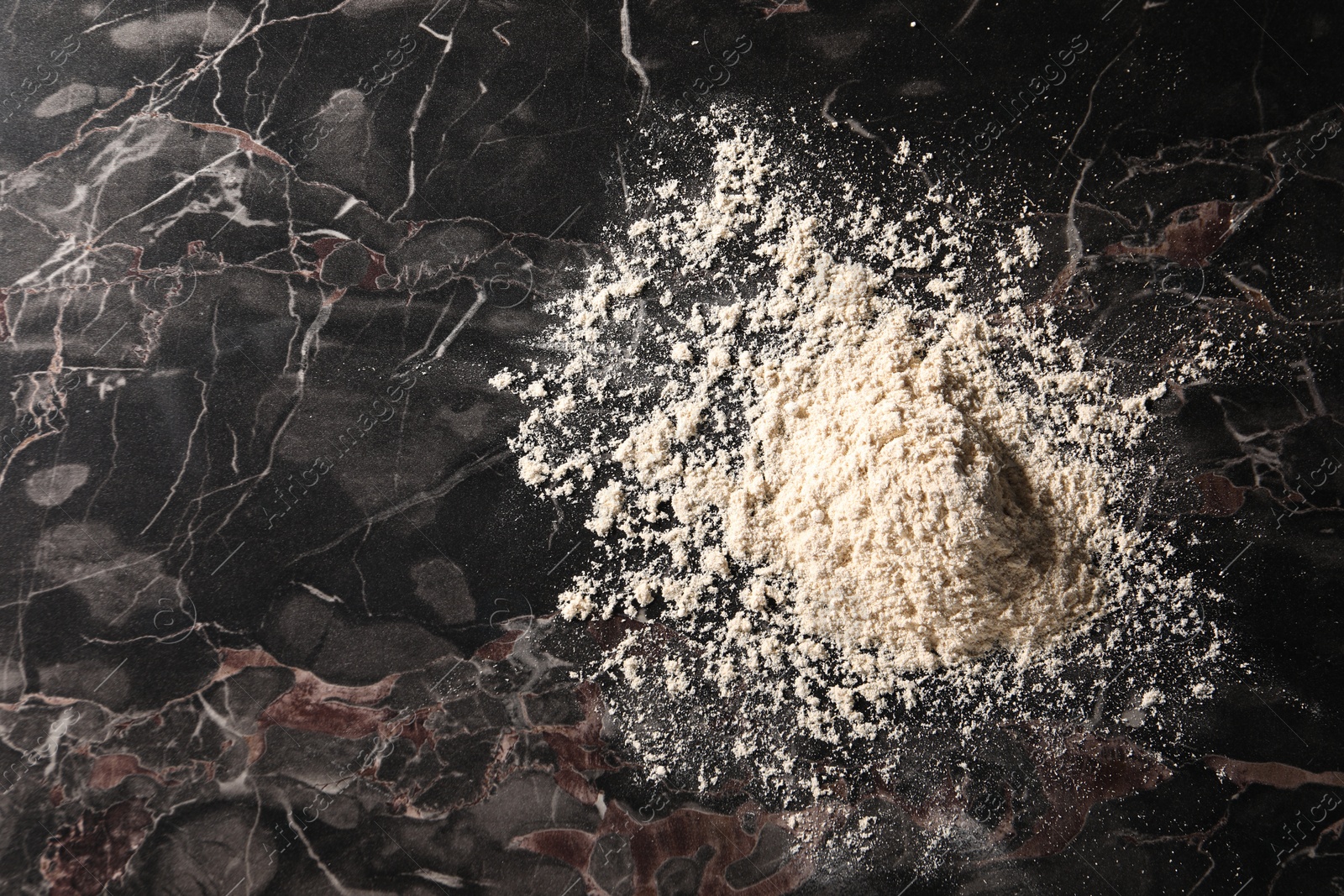 Photo of Pile of flour on black marble table, top view. Space for text