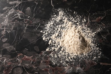 Photo of Pile of flour on black marble table, top view. Space for text