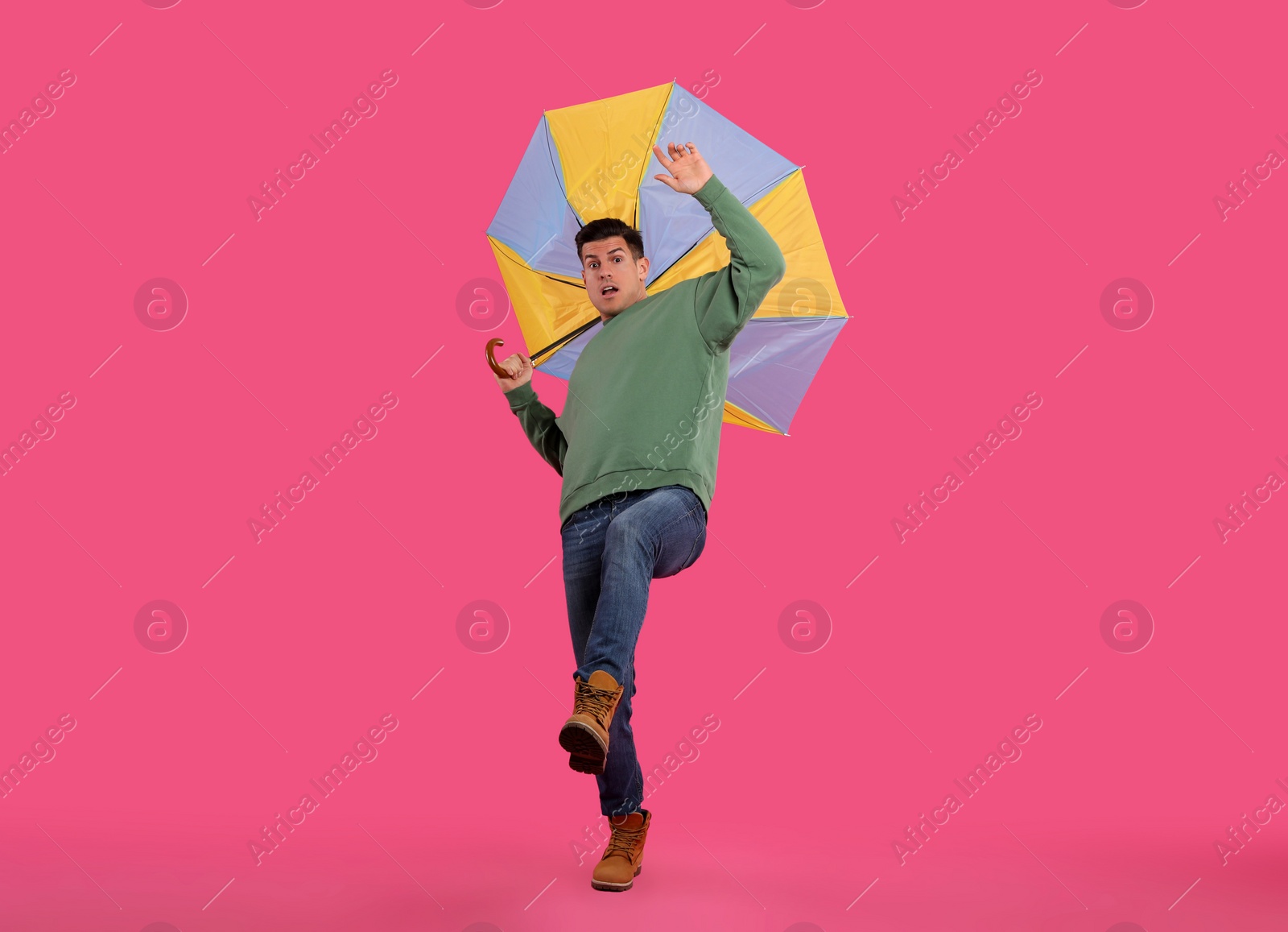 Photo of Emotional man with umbrella caught in gust of wind on pink background