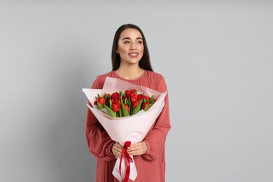Photo of Happy woman with red tulip bouquet on light grey background. 8th of March celebration