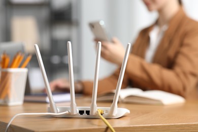 Photo of Woman with smartphone at table indoors, focus on Wi-Fi router