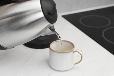 Photo of Pouring hot water from electric kettle into cup in kitchen, closeup