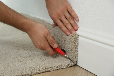 Photo of Worker with cutter knife installing new carpet indoors, closeup