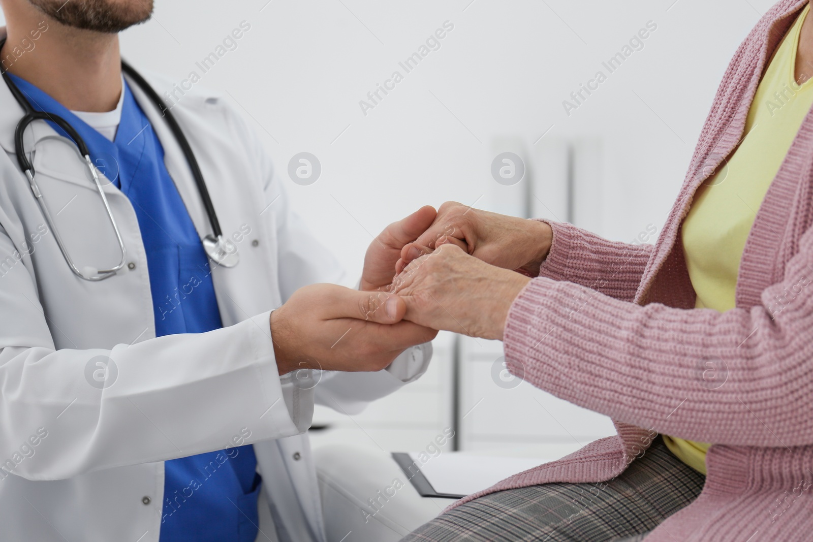 Photo of Doctor holding senior patient's hands in office, closeup