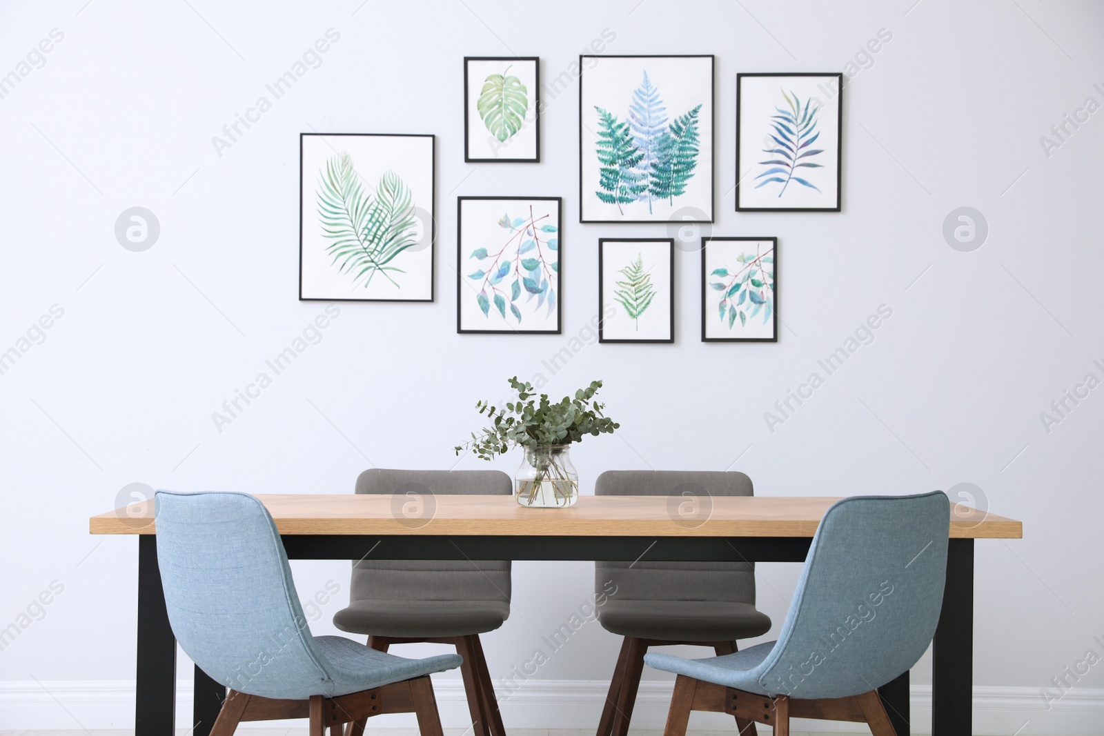 Photo of Stylish room interior with modern table, chairs and paintings of tropical leaves. Idea for design