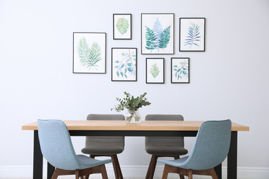 Stylish room interior with modern table, chairs and paintings of tropical leaves. Idea for design