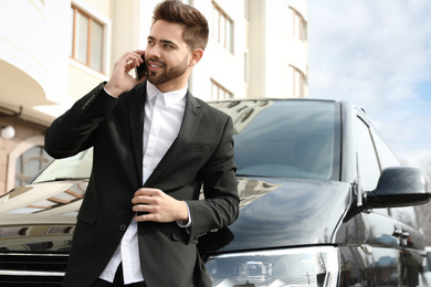 Handsome man talking on smartphone near modern car outdoors