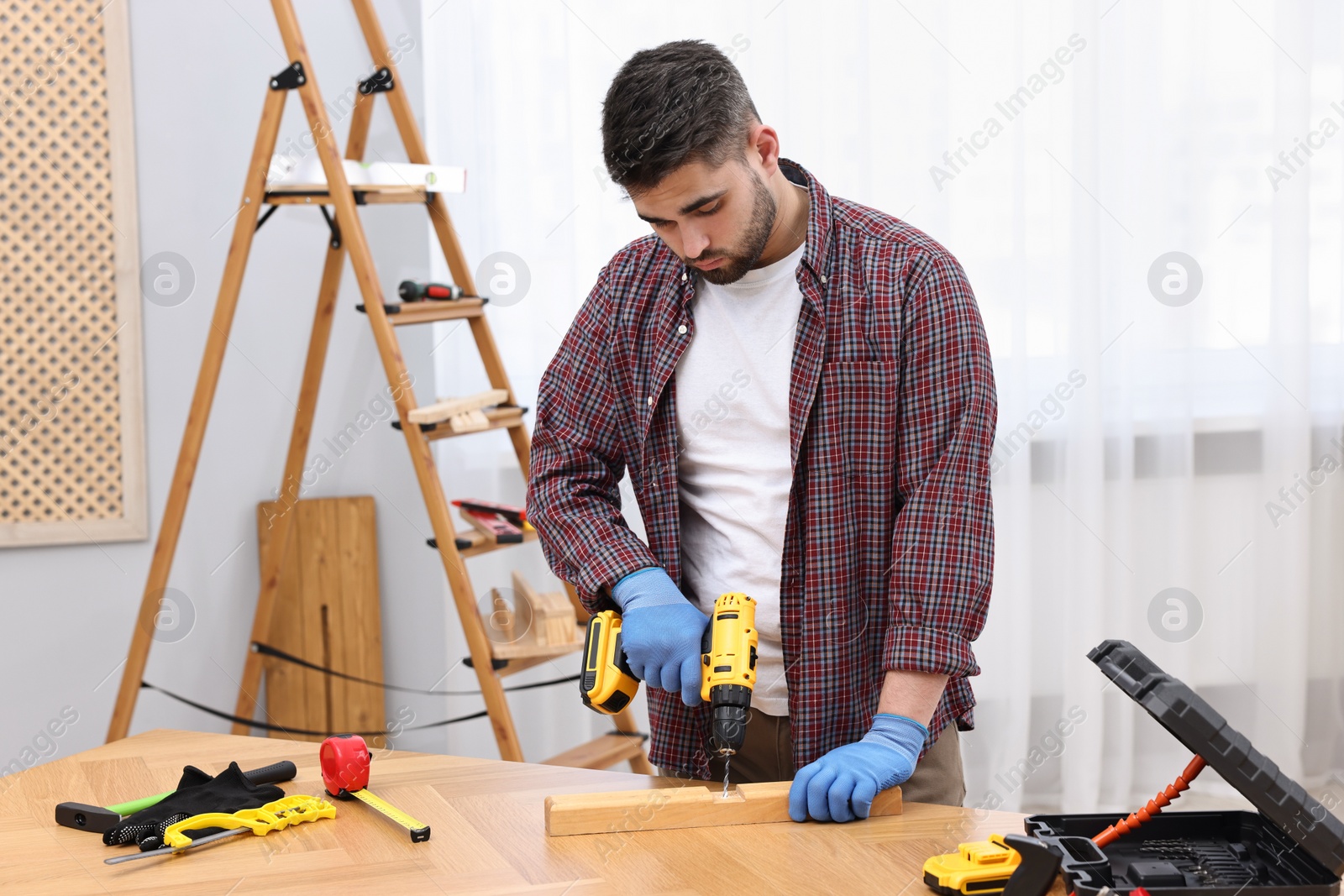 Photo of Young handyman working with electric drill at table in workshop