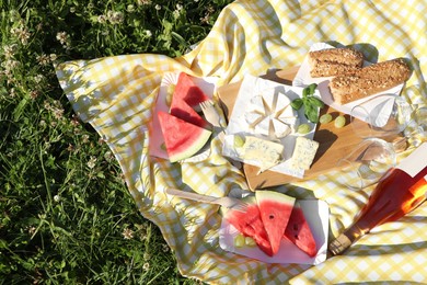 Photo of Picnic blanket with delicious food and wine on green grass outdoors, top view