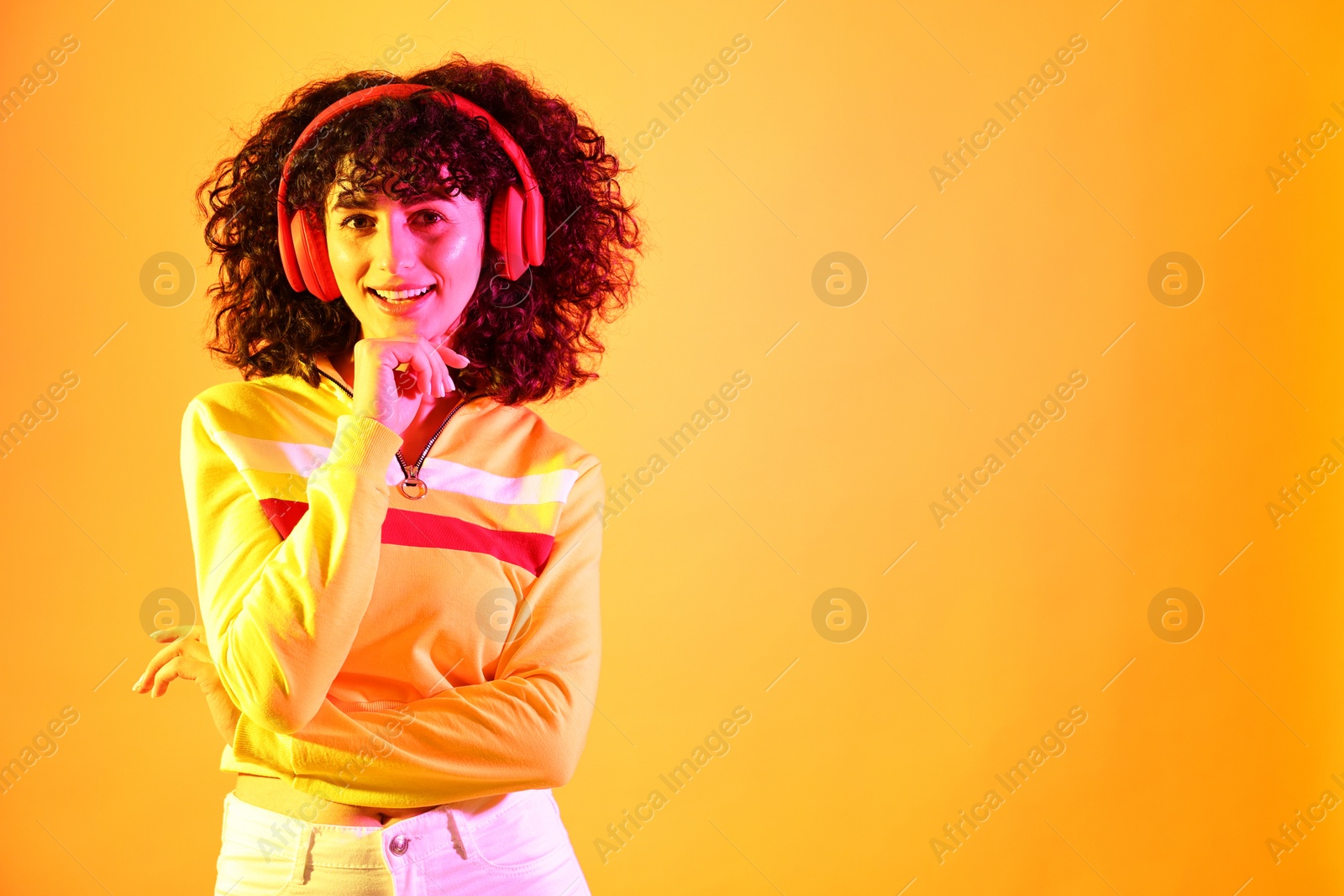 Photo of Beautiful young woman listening to music with headphones on color background in neon lights. Space for text