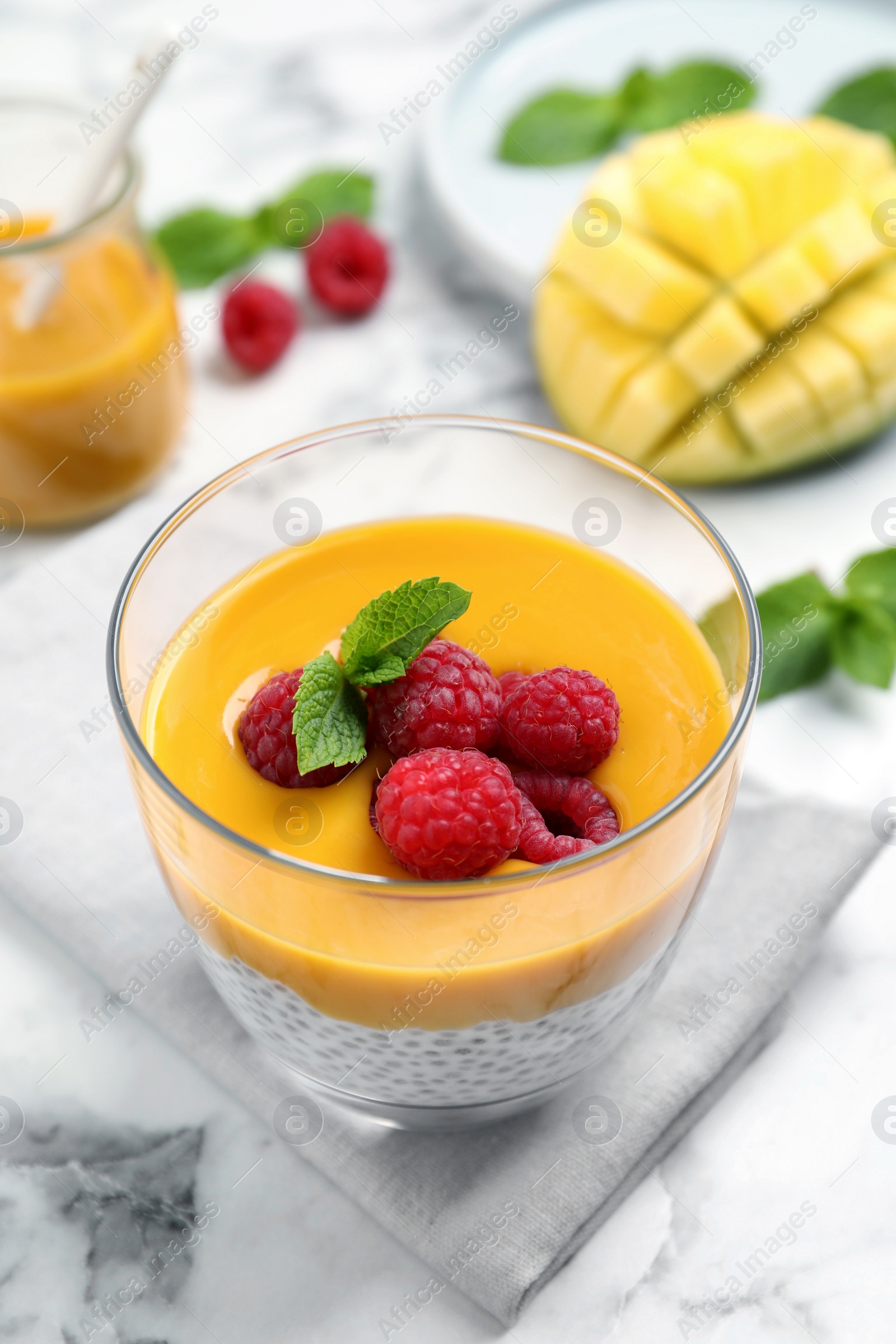 Photo of Delicious chia pudding with mango sauce and raspberries on white marble table