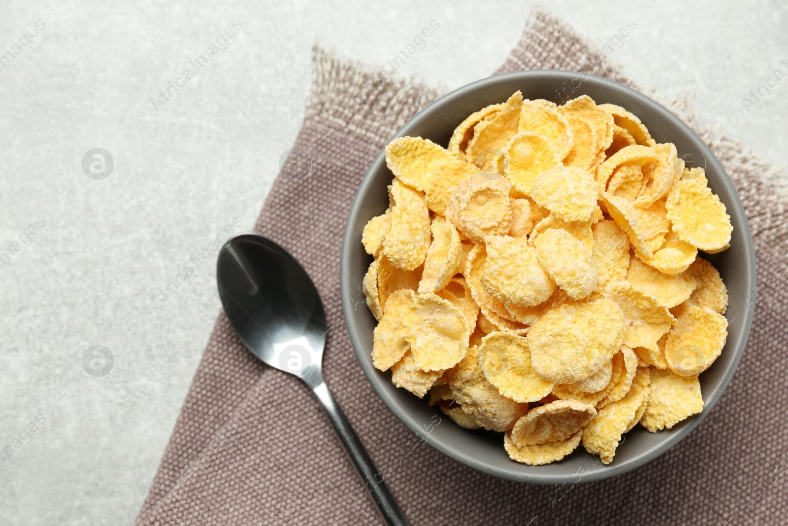 Photo of Bowl of sweet crispy corn flakes on light grey table, flat lay. Breakfast cereal