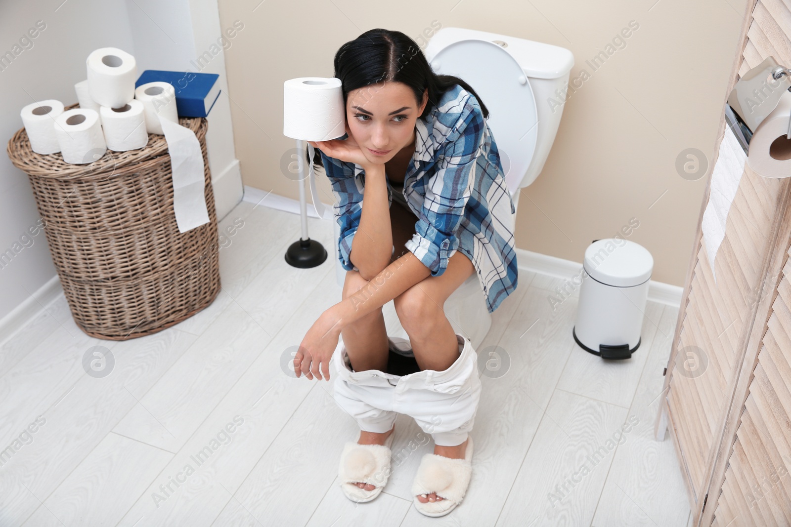 Photo of Woman with paper roll sitting on toilet bowl in bathroom