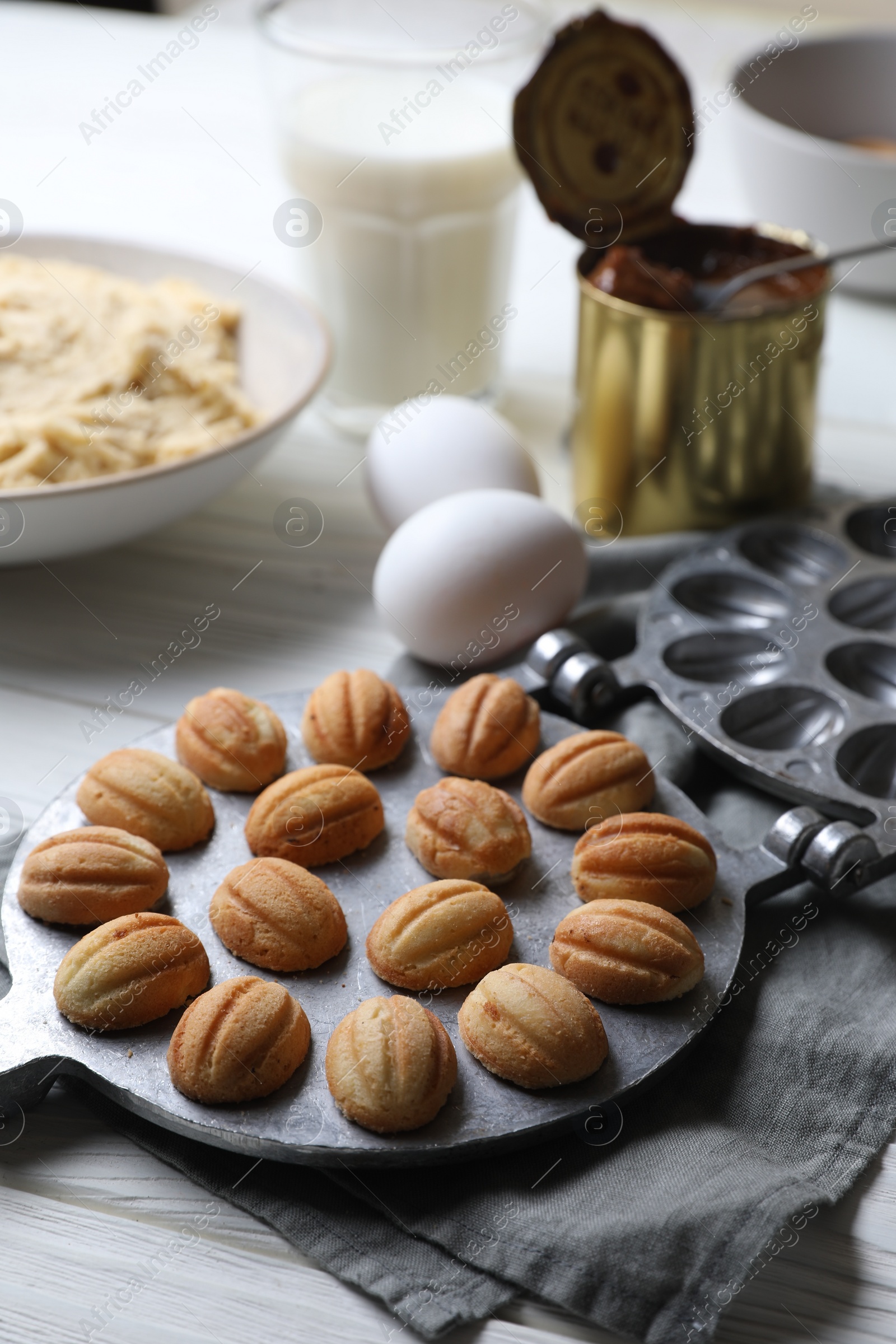 Photo of Delicious walnut shaped cookies with condensed milk and ingredients on white wooden table, closeup