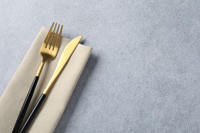 Stylish golden cutlery and napkin on grey table, top view. Space for text