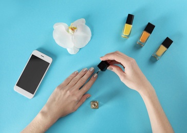 Woman applying nail polish on color background, top view