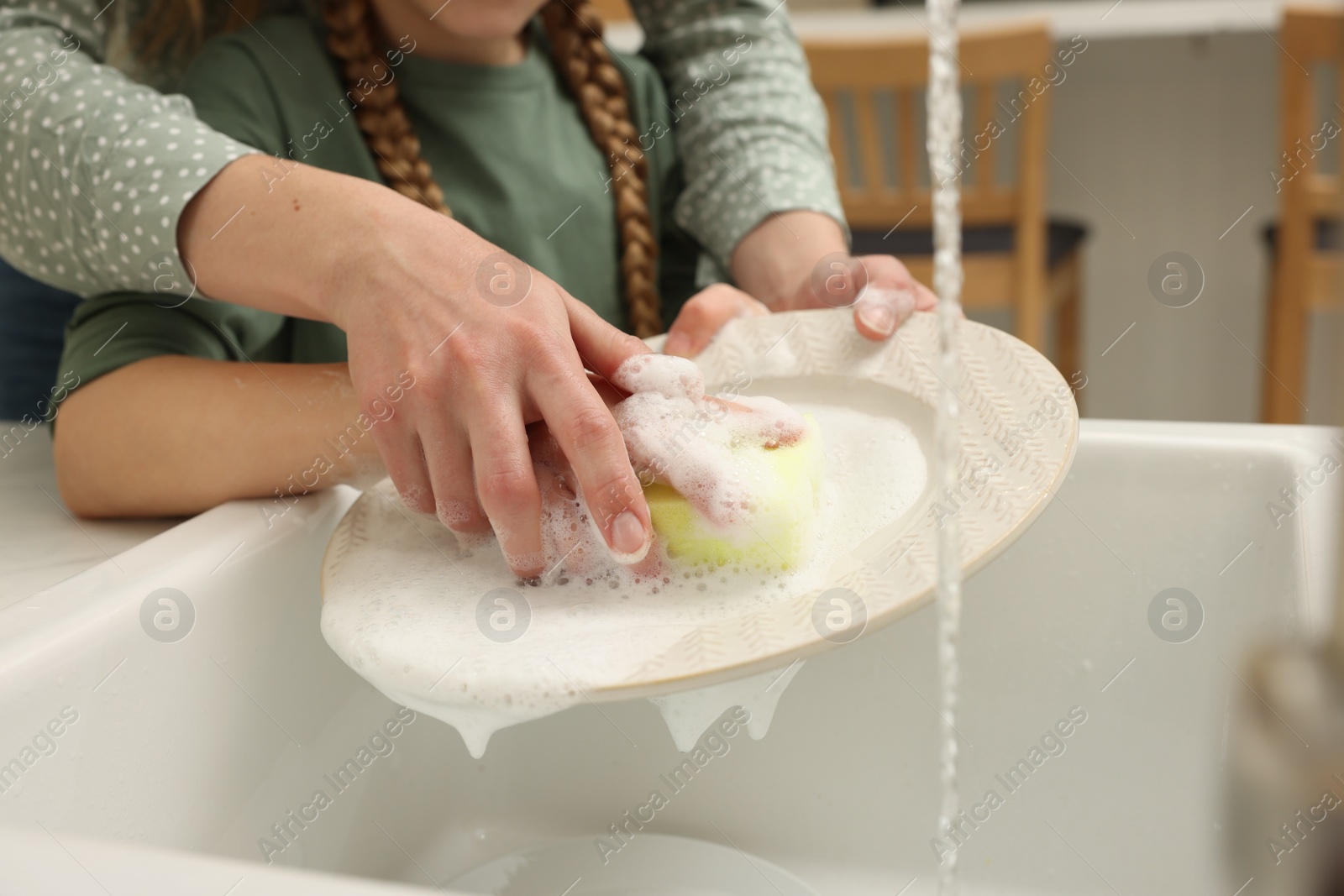 Photo of Mother and daughter washing plate above sink indoors, closeup