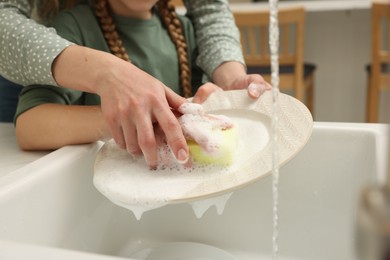 Photo of Mother and daughter washing plate above sink indoors, closeup