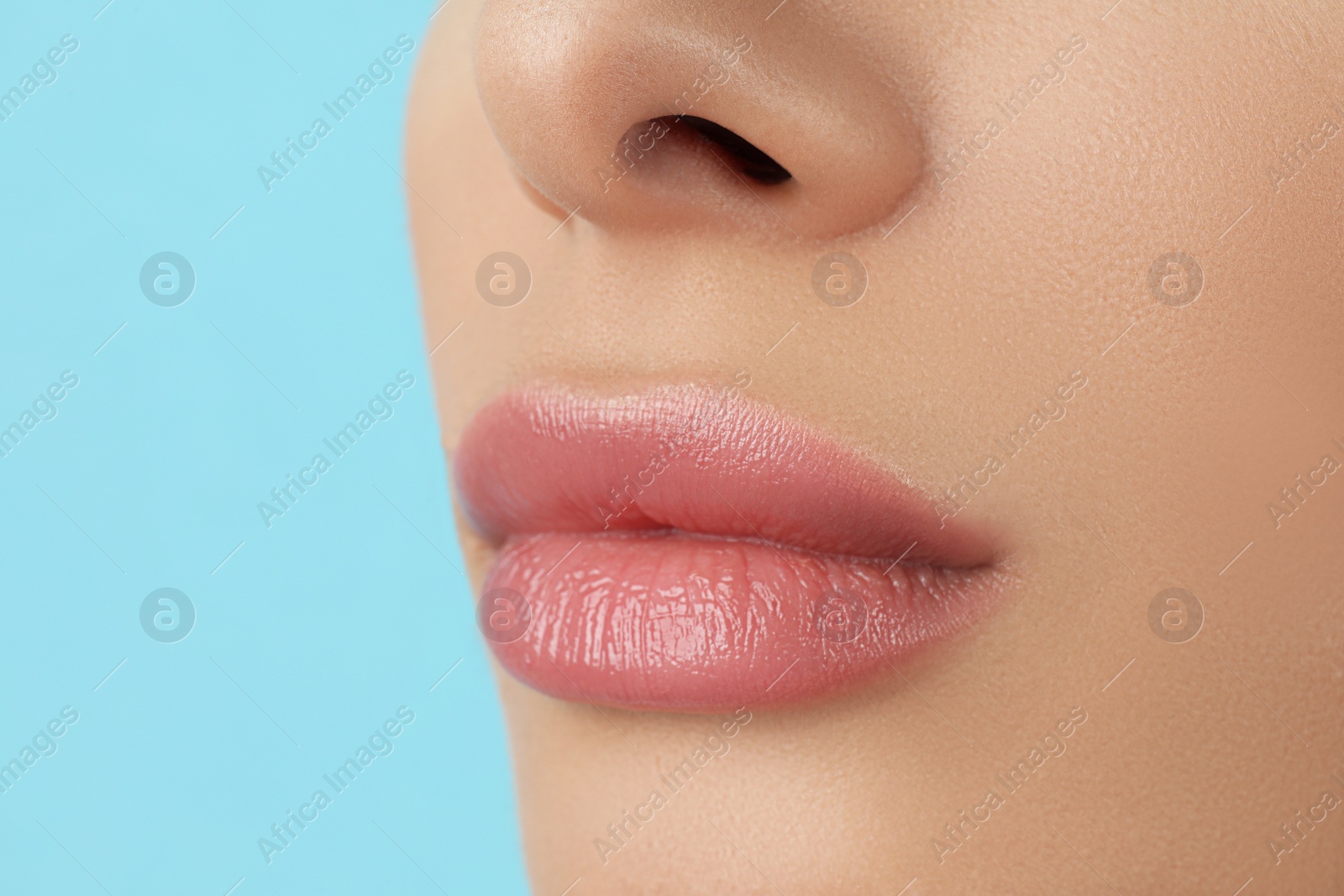 Photo of Woman with beautiful full lips on light blue background, closeup