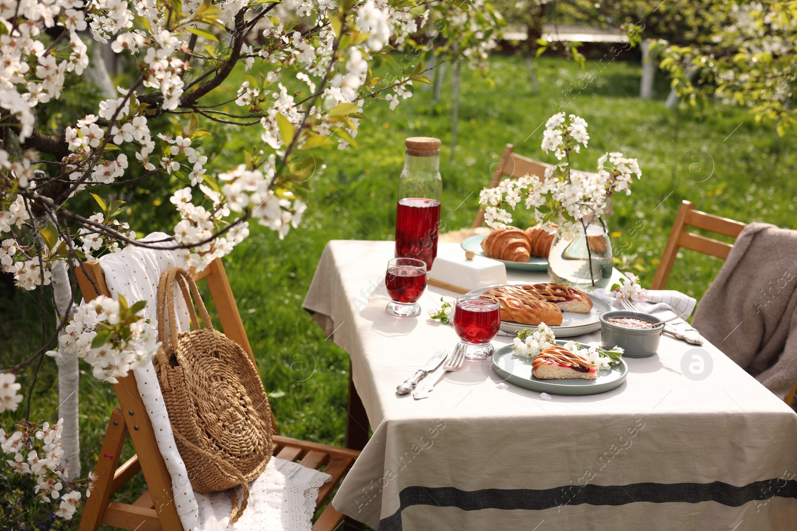 Photo of Stylish table setting with beautiful spring flowers, fruit drink and pie in garden