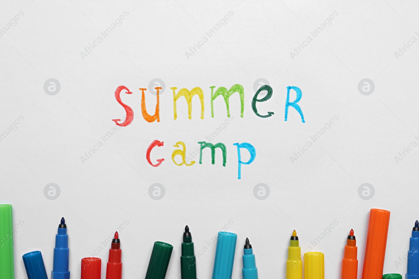 Photo of Text SUMMER CAMP and colorful felt tip pens on white paper, flat lay