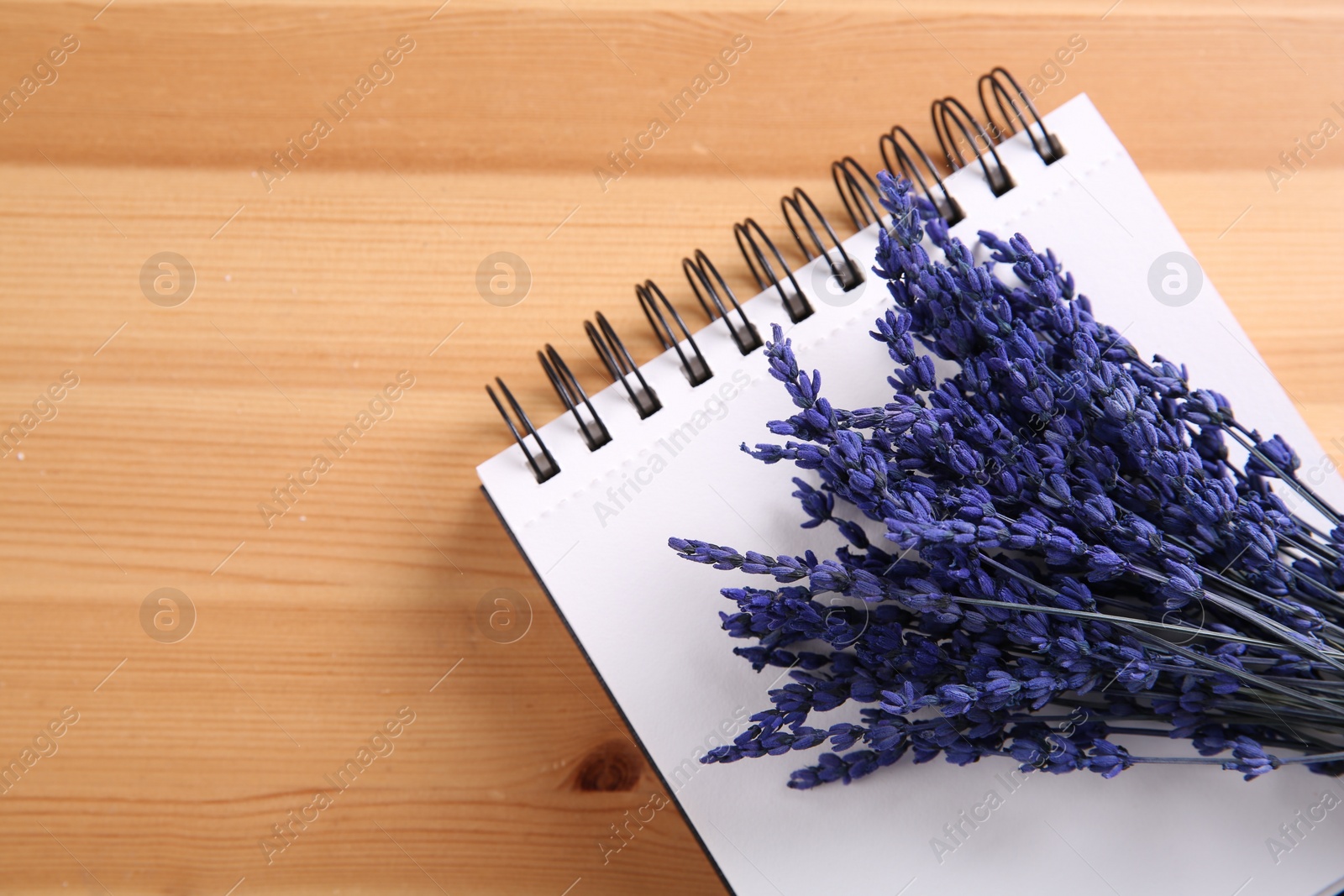 Photo of Bouquet of beautiful preserved lavender flowers and notebook on wooden table, top view. Space for text