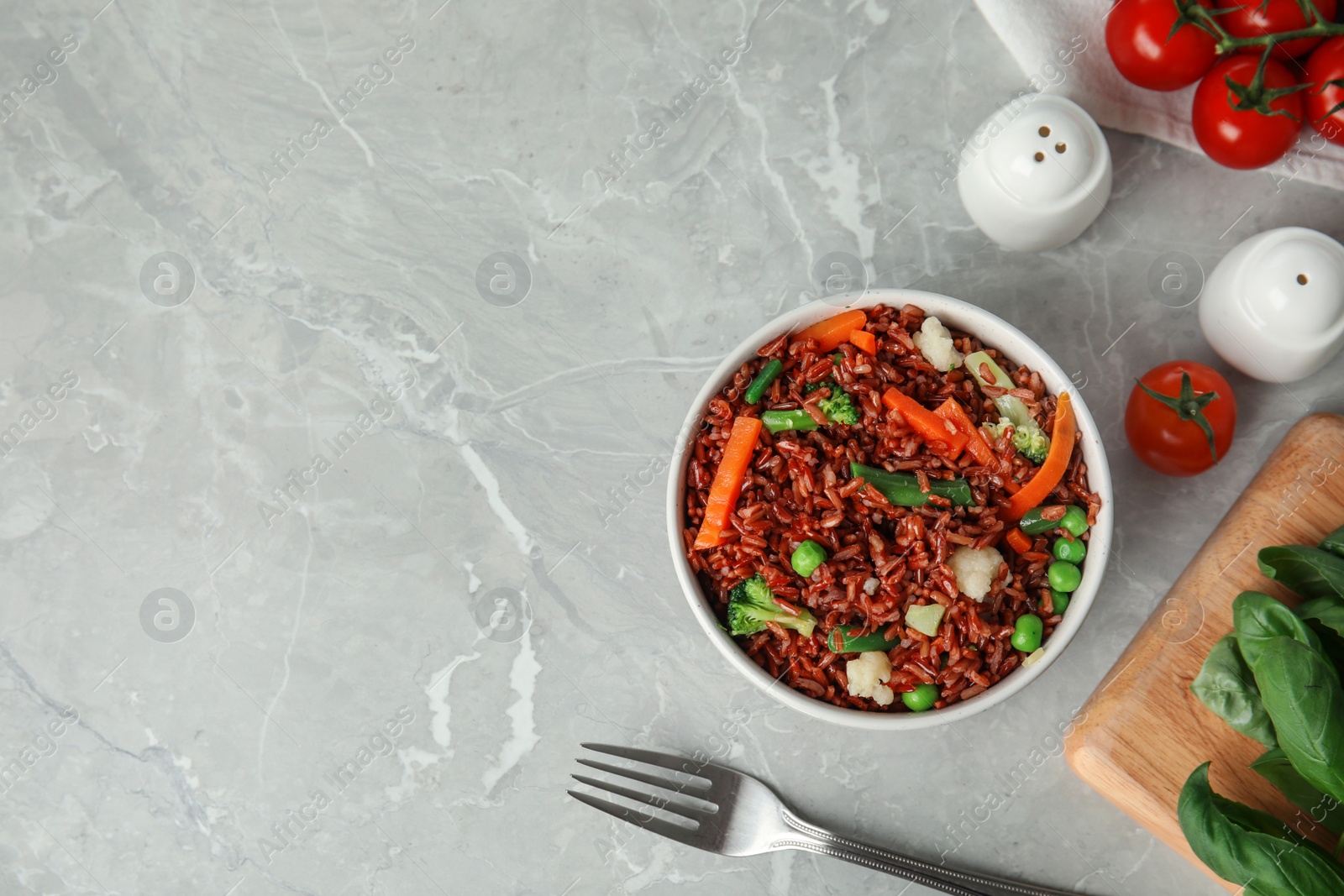 Photo of Bowl of brown rice with vegetables on grey table, flat lay. Space for text