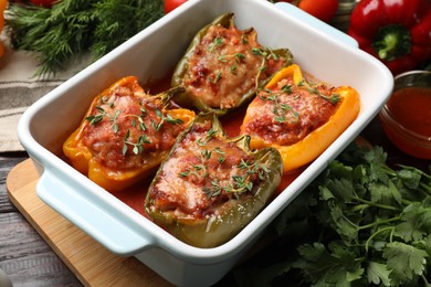 Photo of Tasty stuffed peppers in dish and ingredients on wooden table, closeup