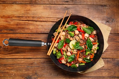 Photo of Stir-fry. Tasty noodles with meat in wok and chopsticks on wooden table, top view