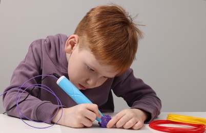 Photo of Boy drawing with stylish 3D pen at white table