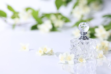 Photo of Aromatic perfume in bottle and beautiful jasmine flowers on white background, space for text