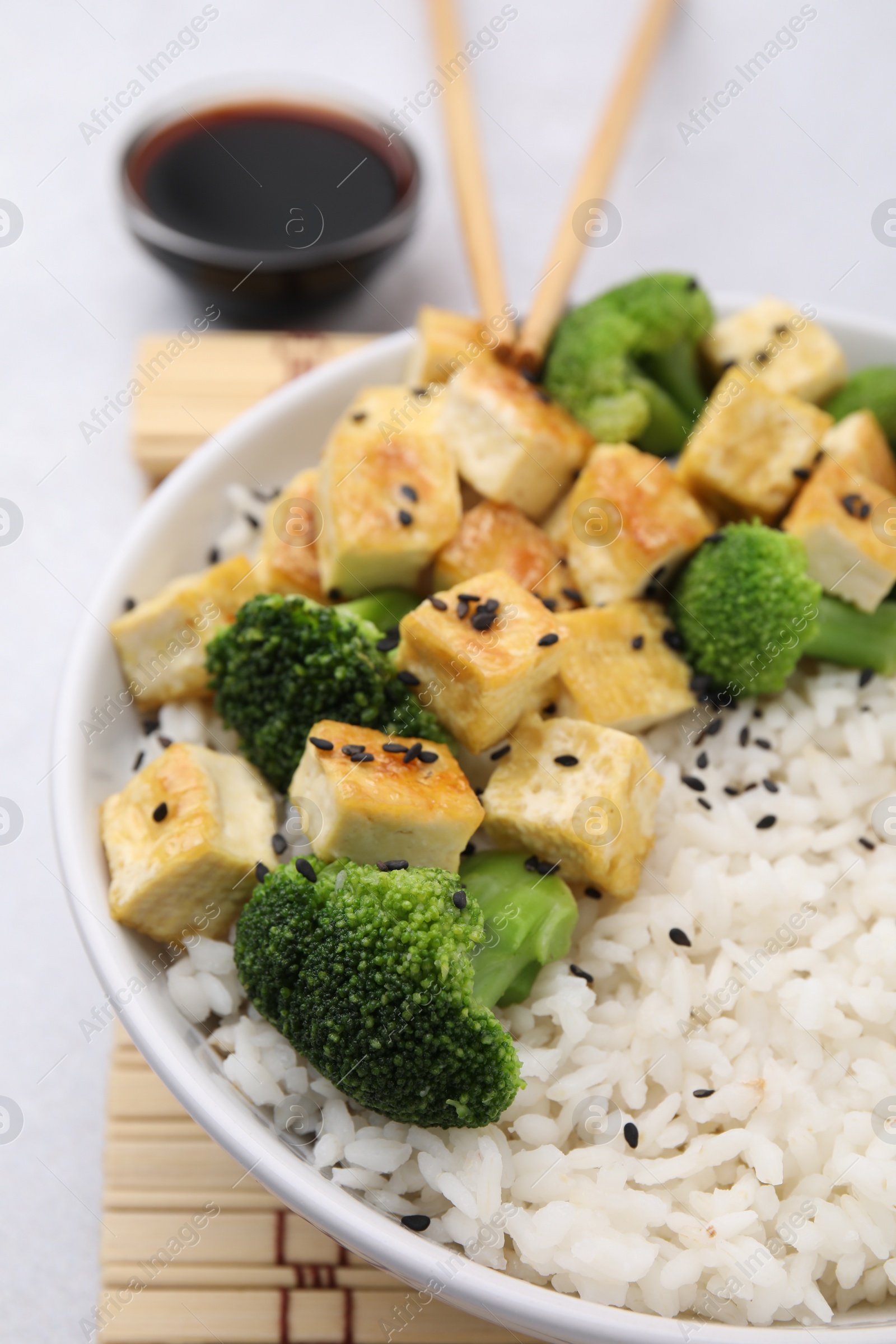 Photo of Bowl of rice with fried tofu and broccoli on white table, closeup