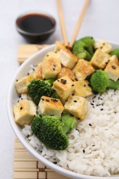 Photo of Bowl of rice with fried tofu and broccoli on white table, closeup