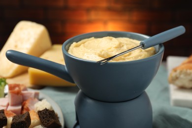 Photo of Tasty melted cheese in fondue pot, fork and snacks on table, closeup