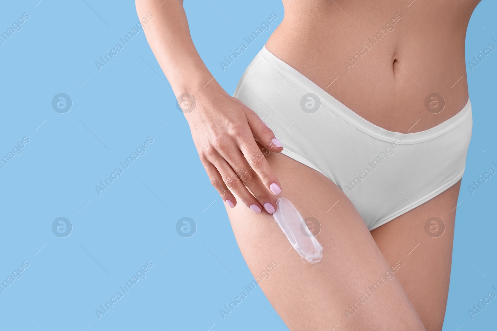 Photo of Woman with smear of body cream on her leg against light blue background, closeup. Space for text