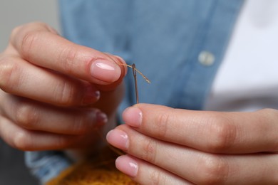 Photo of Woman inserting thread through eye of needle, closeup