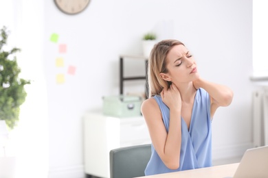 Photo of Young woman suffering from neck pain in office