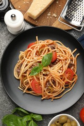 Photo of Delicious pasta with anchovies, tomatoes and olives on grey table, flat lay