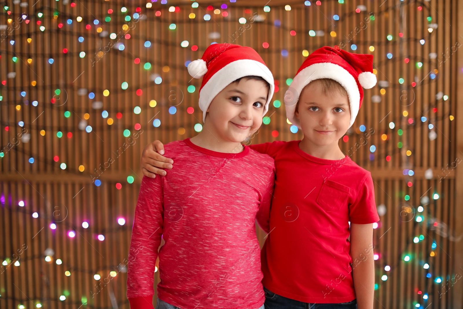 Photo of Cute little children in Santa hats on blurred lights background. Christmas celebration