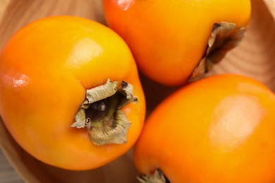 Photo of Delicious ripe persimmons in wooden bowl, top view